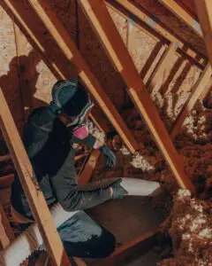 Mammoth Home Renovations team member removing old insulation from an attic space