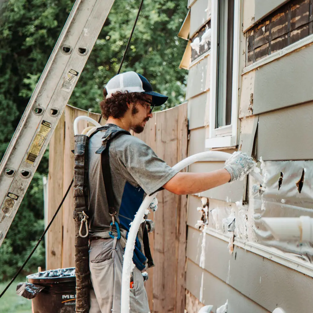 Injection Foam Expert from Mammoth Home Renovations installing RetroFoam insulation in an exterior wall of a white house.